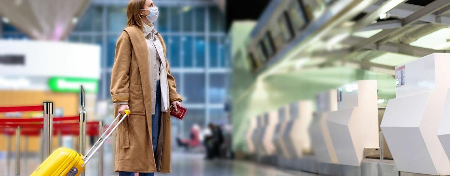 Woman wearing a surgical mask, with luggage at the airport.