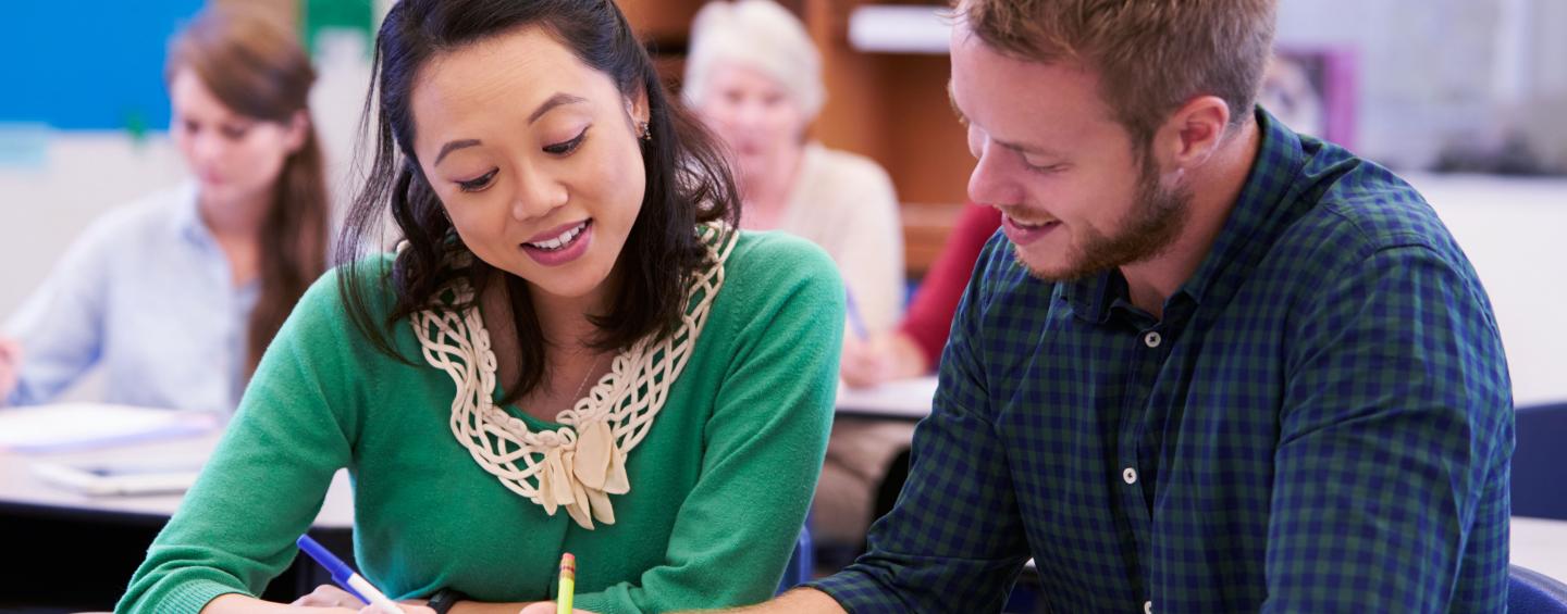 man and woman in class looking at book